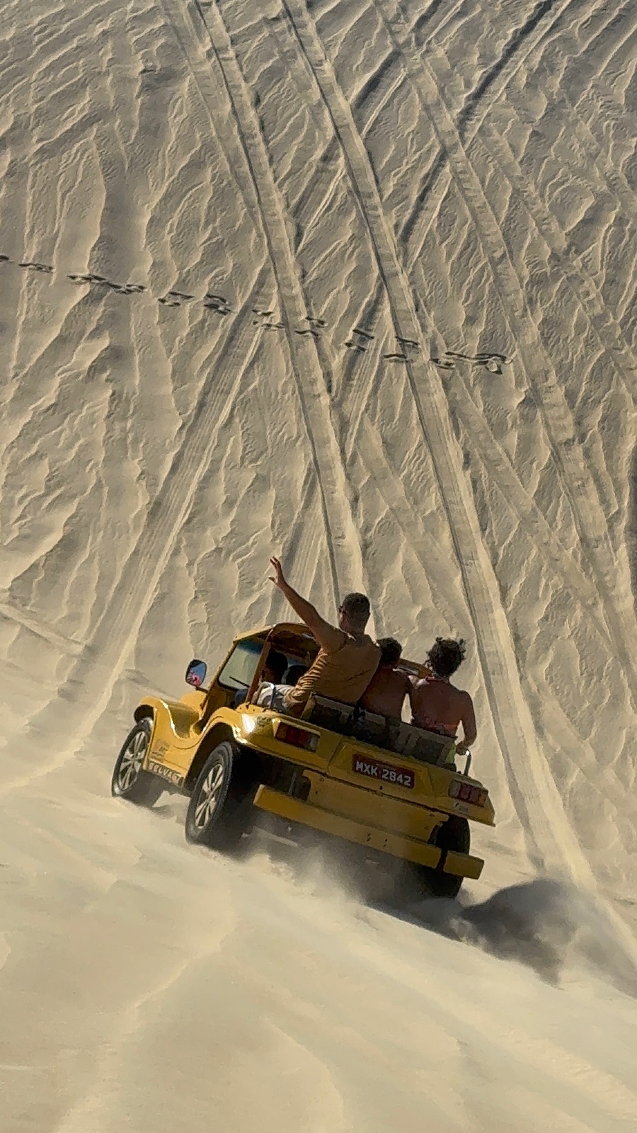 Buggy amarelo subindo uma duna de areia com turistas a bordo